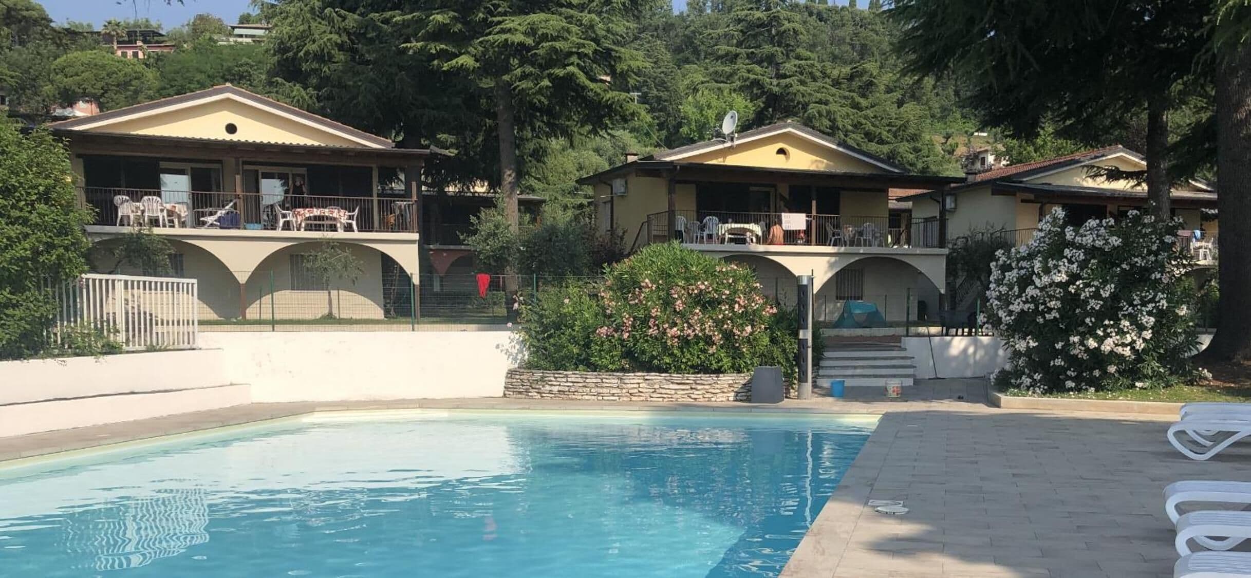 Una piscina con borde de baldosas, rodeada de casas de dos pisos con balcones y mobiliario exterior.