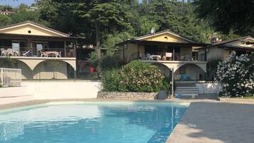Una piscina con borde de baldosas, rodeada de casas de dos pisos con balcones y mobiliario exterior.