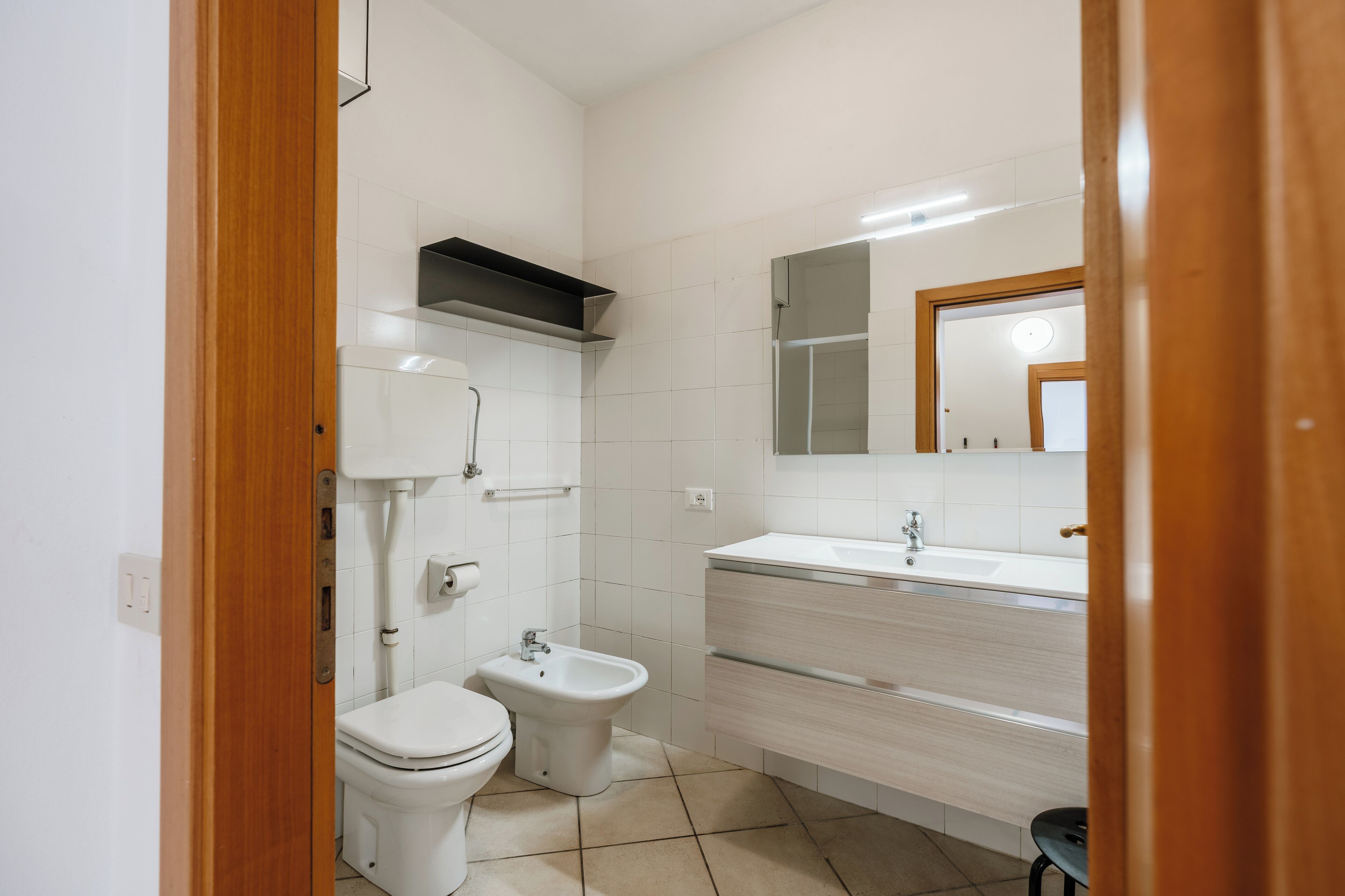 A compact bathroom with a toilet, bidet, and a vanity with a mirror.
