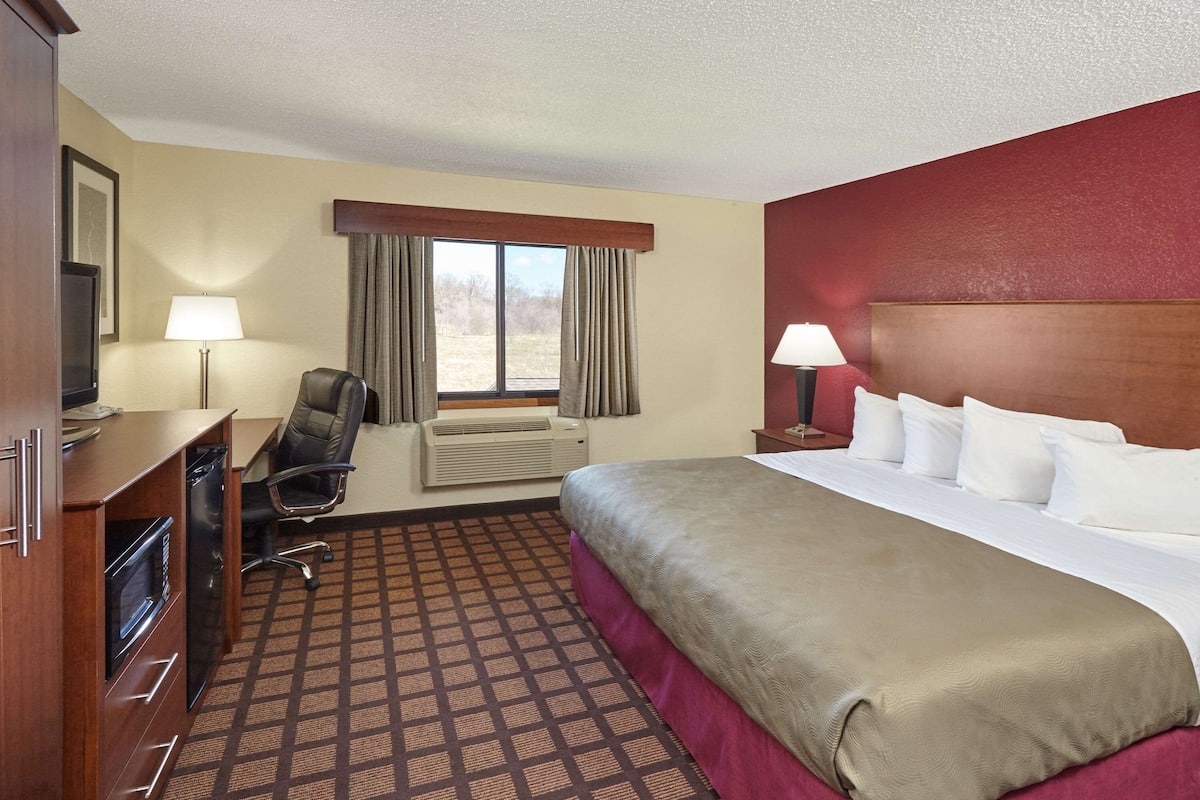 A hotel room with a bed, desk, chair, and a window with curtains.