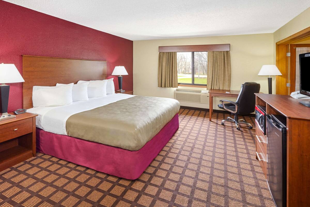 A hotel room with a large bed, a desk with a chair, a television, and a window with curtains.