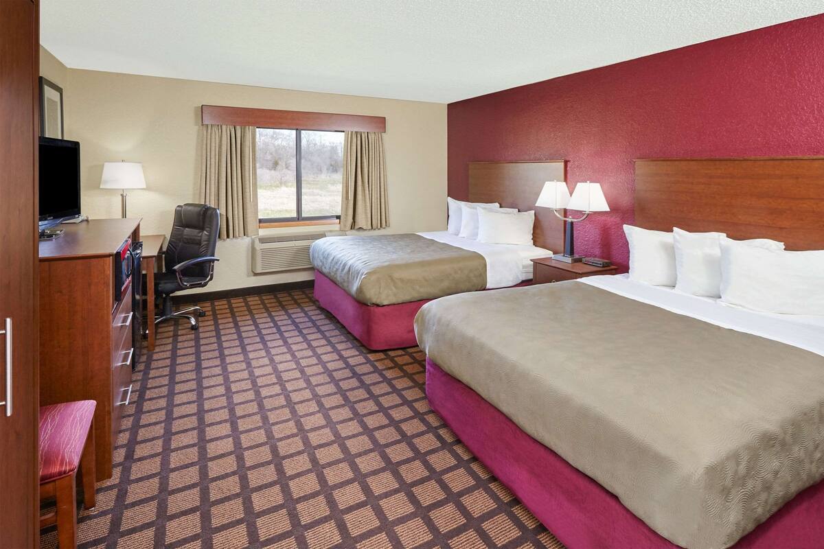 A hotel room with two beds, a desk with a chair, a television, and a window with curtains.