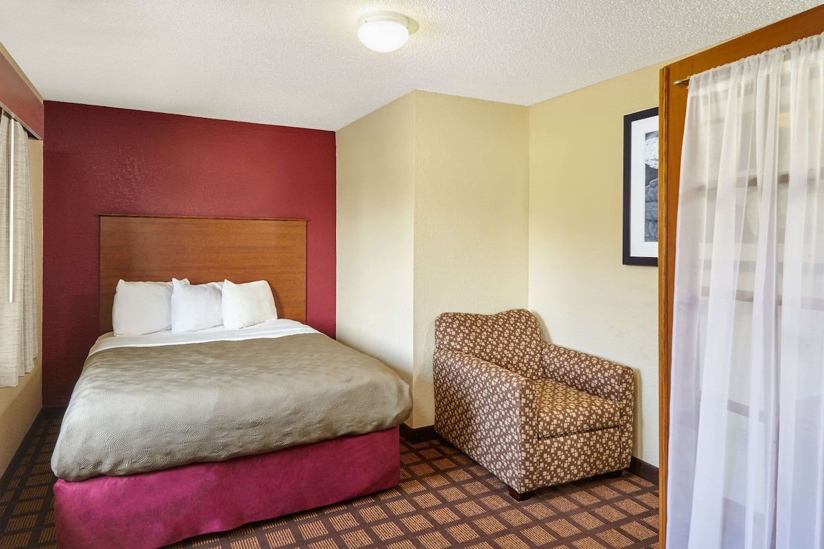 A hotel room with a bed, a chair, and a picture on the wall.