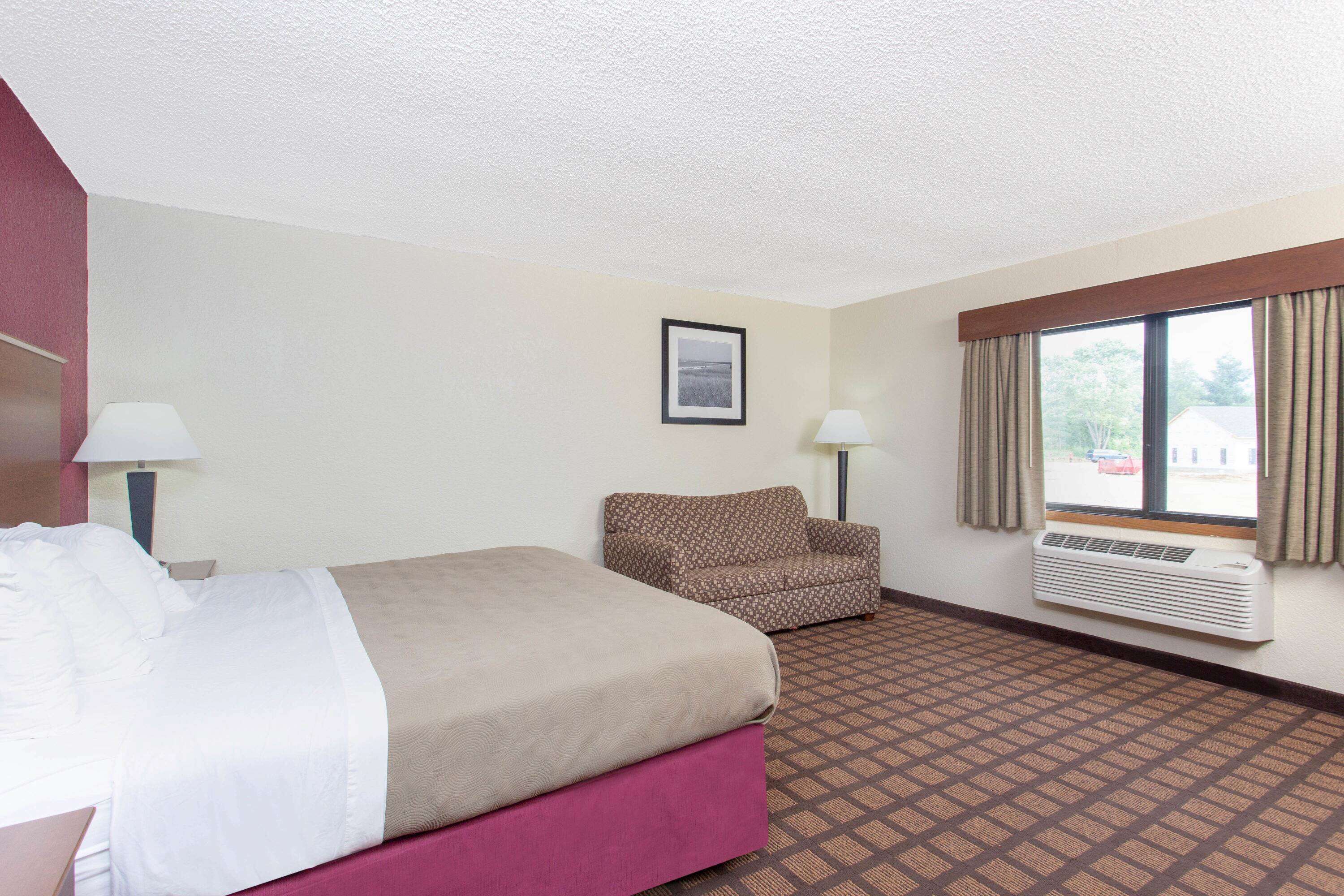 Ein Hotelzimmer mit einem Bett, einem Sessel, einem Fenster mit Vorhängen und einer Klimaanlage.
