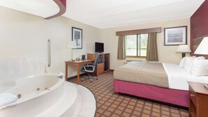Een hotelkamer met een groot bad, een bed met een roze dekbedovertrek, een bureau met een computer en een raam met gordijnen.