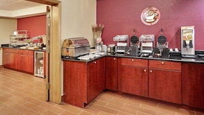 Een hotelkeuken met rode kastjes, een koffiehoek en een koelkast.