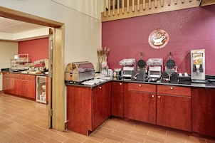 A hotel kitchen with red cabinets, a coffee station, and a refrigerator.