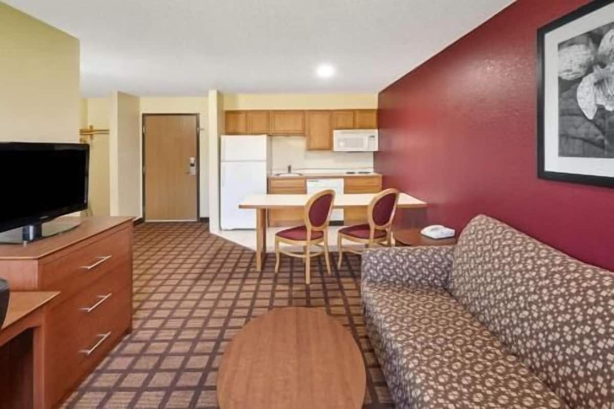 A compact living space with a sofa, a TV, a dining area with chairs, and a kitchen with a microwave.