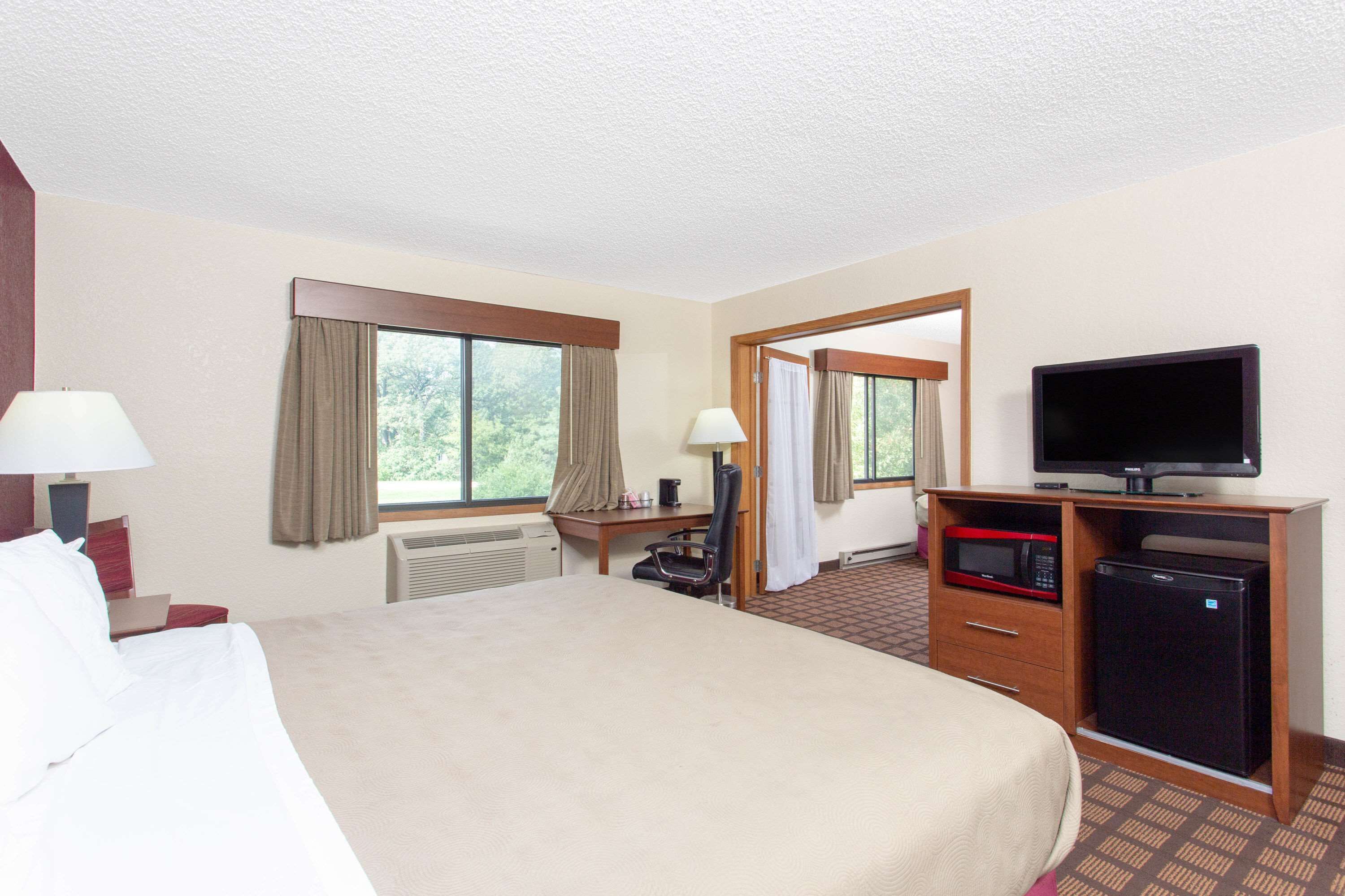 Quarto de hotel com uma cama grande, uma escrivaninha com computador, televisão e frigorífico.