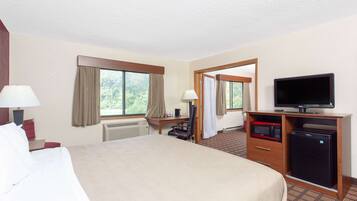 Quarto de hotel com uma cama grande, uma escrivaninha com computador, televisão e frigorífico.