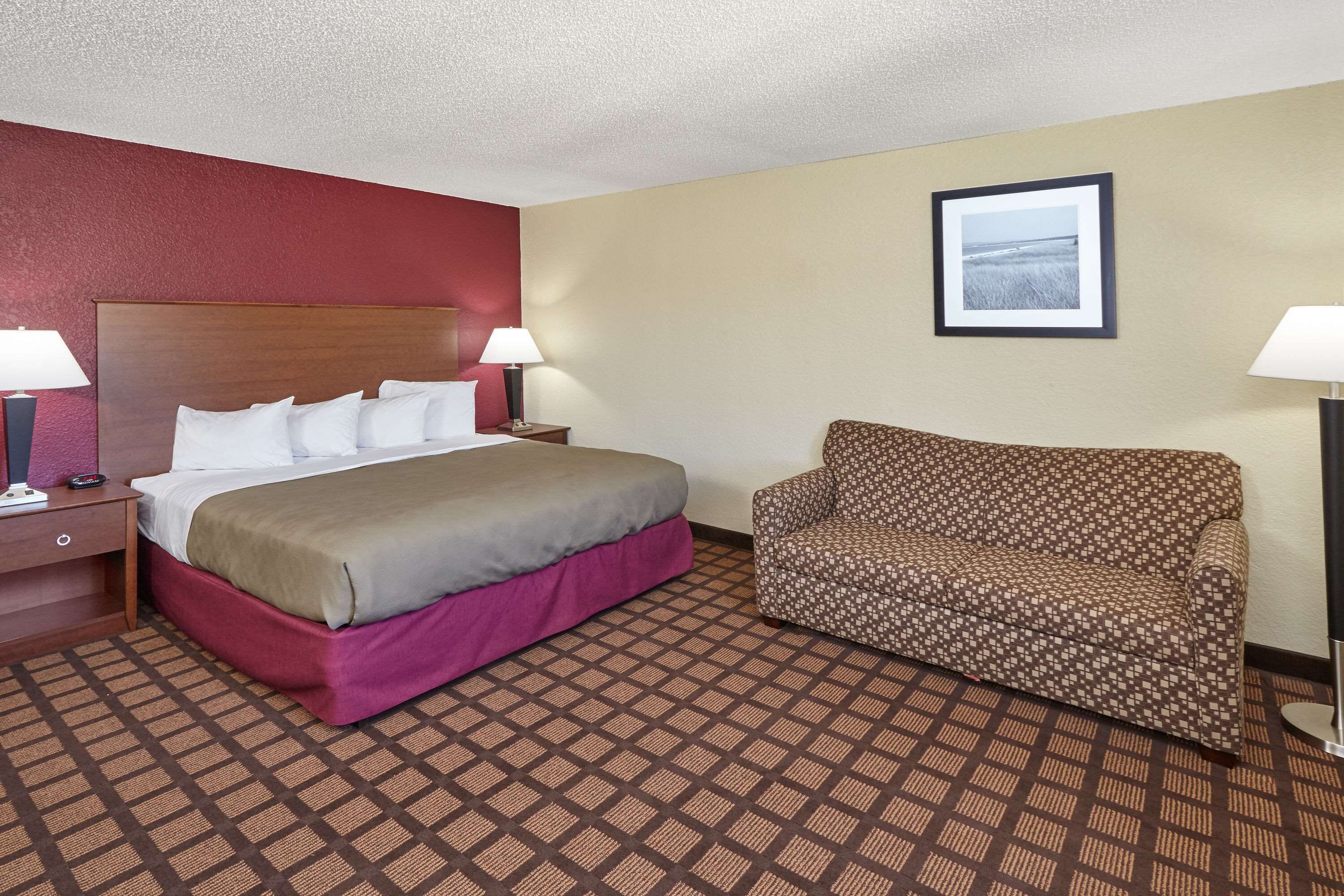 Una habitación de hotel con una cama, un sofá, una mesita de noche y una lámpara.