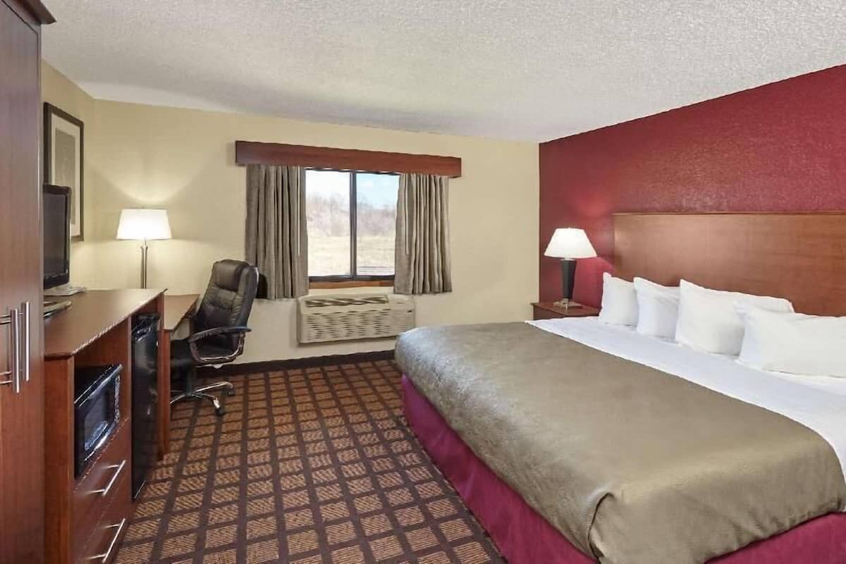 A hotel room with a bed, desk, chair, lamps, and a window.
