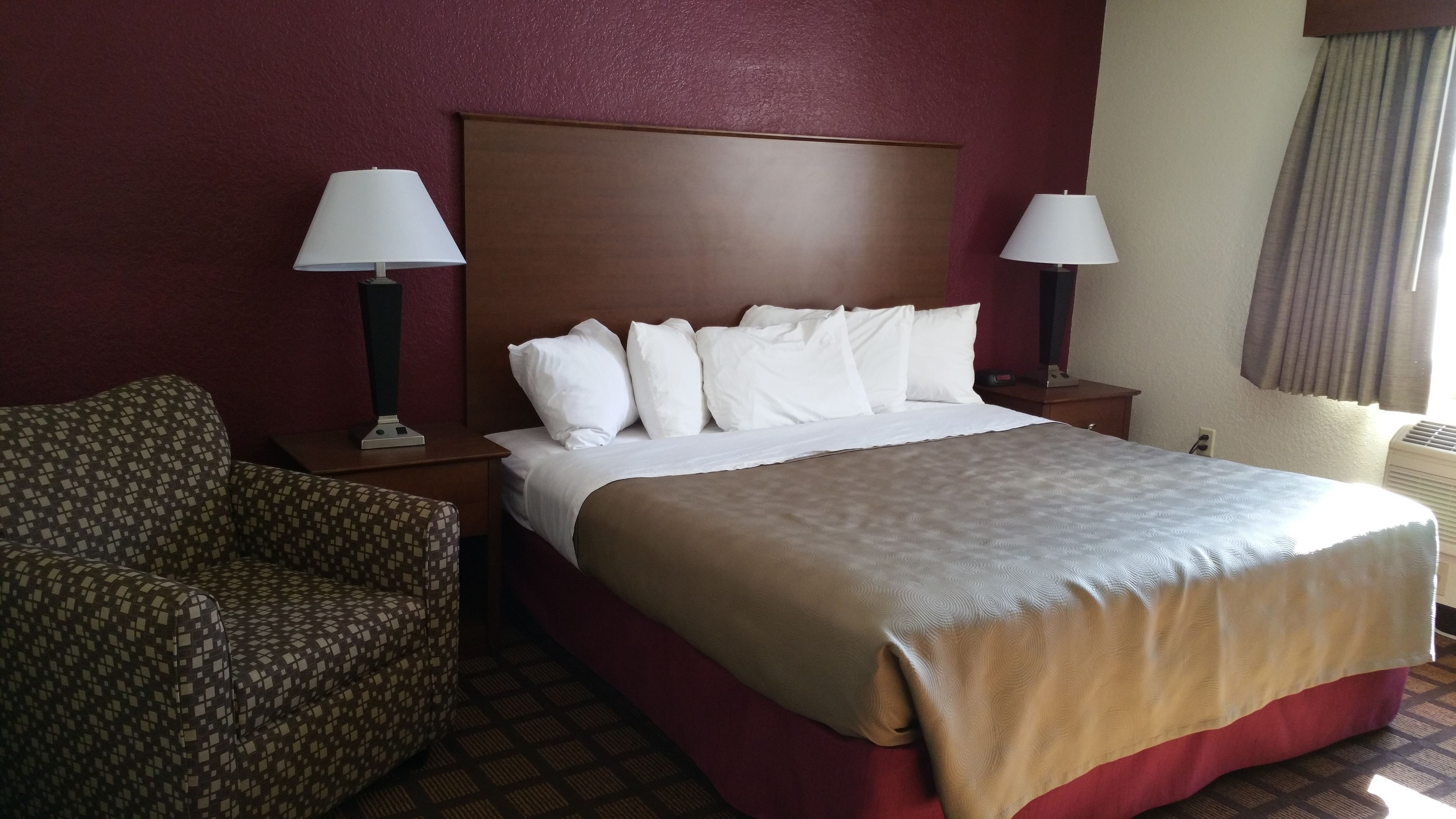 Quarto de hotel com uma cama grande, duas mesas de cabeceira, uma cadeira e uma janela com cortinas.