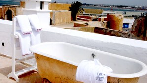 Eine Badewanne mit Handtuch, einem weißen Stuhl und Meerblick.