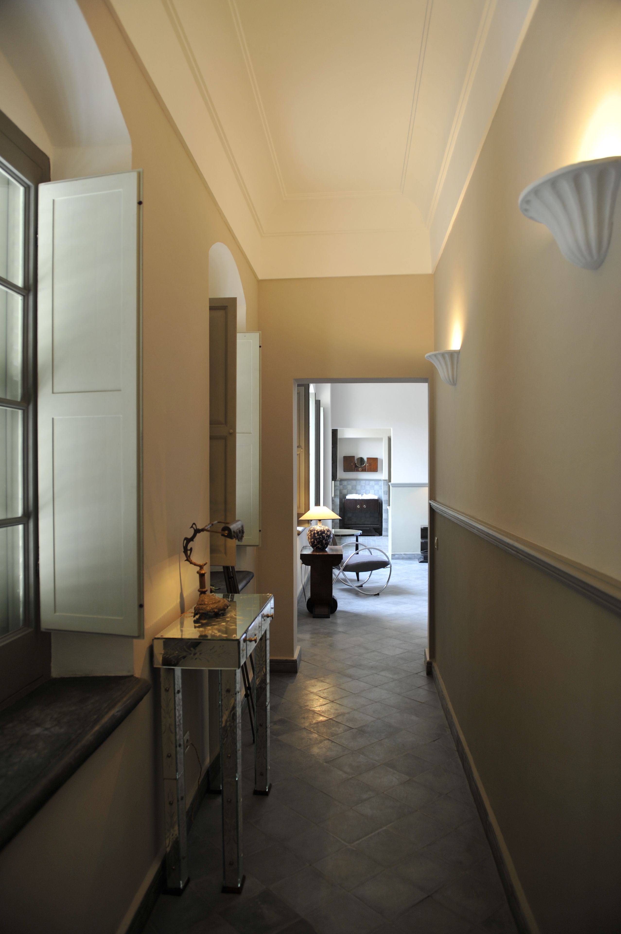 A narrow hallway with a bench, a table with a lamp, and a chair.