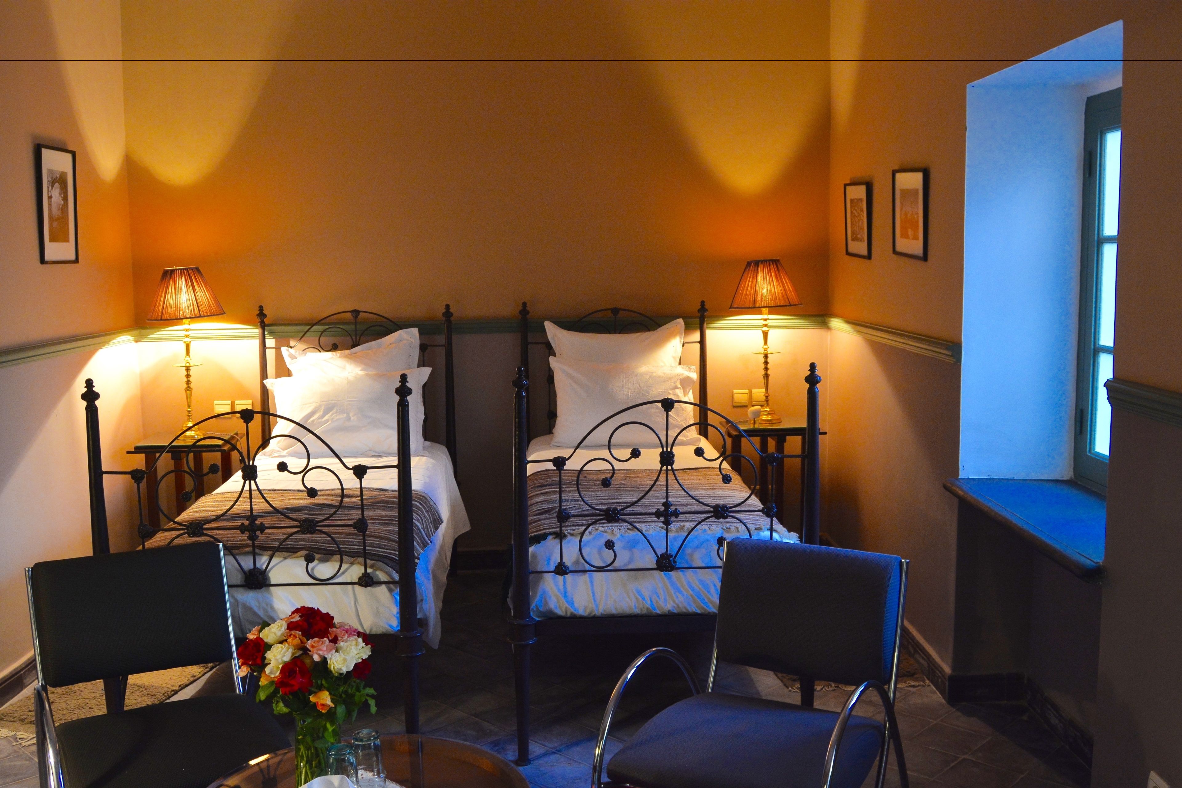 Habitación de hotel con dos camas, una zona de estar con sillas, una mesita con un jarrón de flores y una ventana con vistas.
