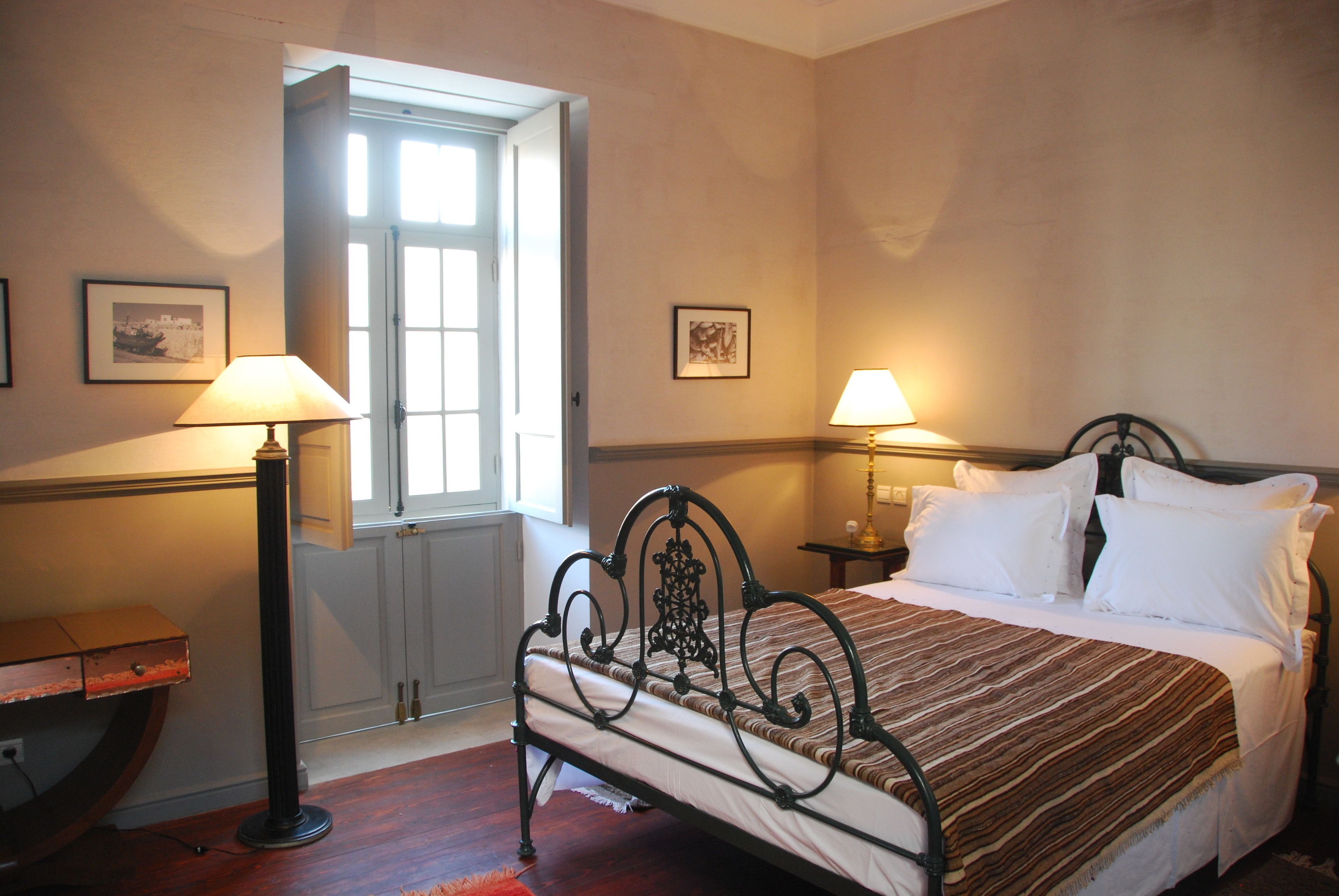 A bedroom with a bed, two bedside lamps, a window, and a door.