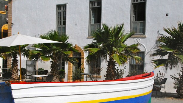 A colorful boat parked in front of a building with multiple windows and a white facade. - Hotel L'Iglesia (El Jadida)