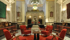 Eine Lobby mit roten Sesseln, die um einen zentralen Tisch angeordnet sind, einem Kronleuchter und Blick auf einen Balkon.