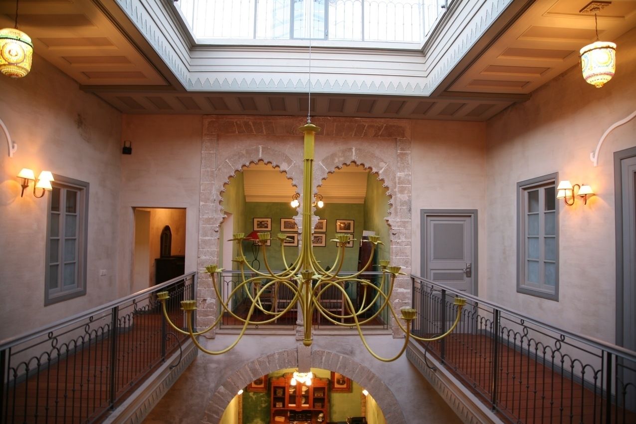 A grand staircase with a chandelier, arched doorways, and wall-mounted lights.