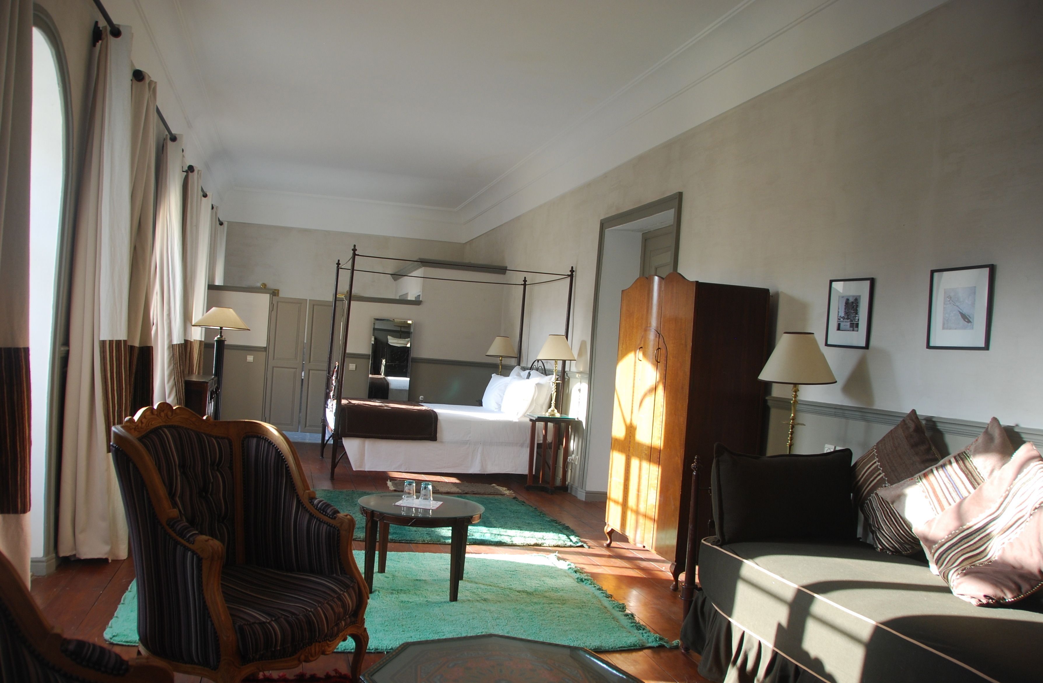 A hotel room with a bed, a sitting area with a sofa and armchair, a small table, and a mirror.