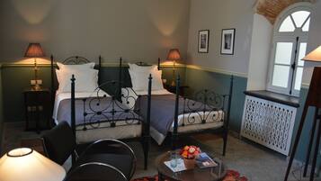 A bedroom with two beds, a sitting area with a table and chairs, and a window with a view.