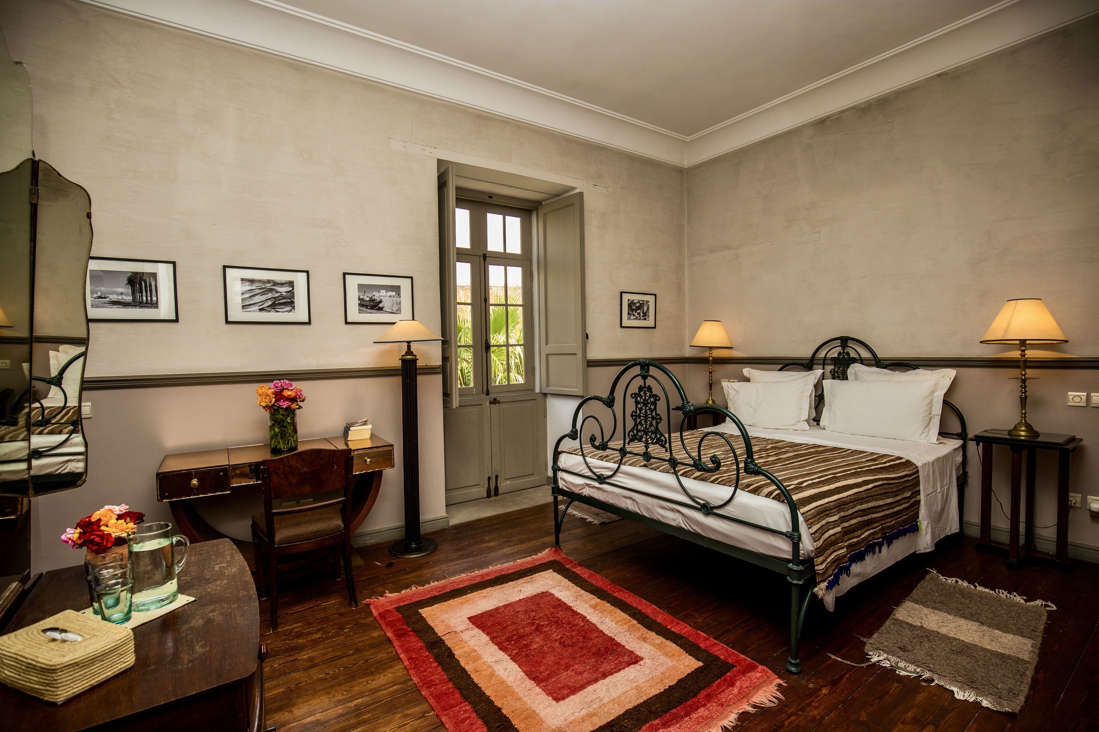A bedroom with a bed, bedside lamps, a desk, a chair, and a window.