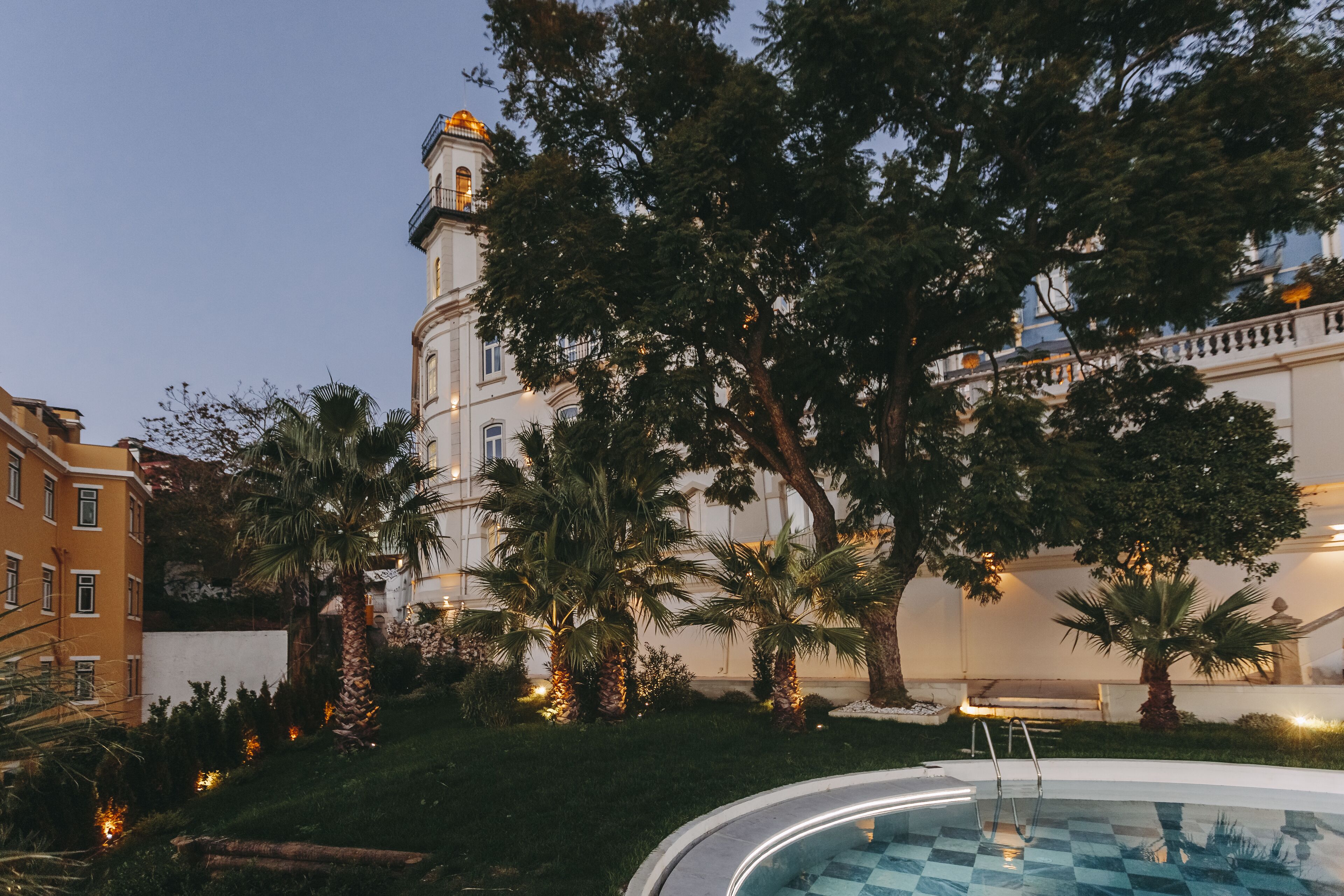 A pool area with a clear view of a large building with a tower, surrounded by palm trees and greenery.