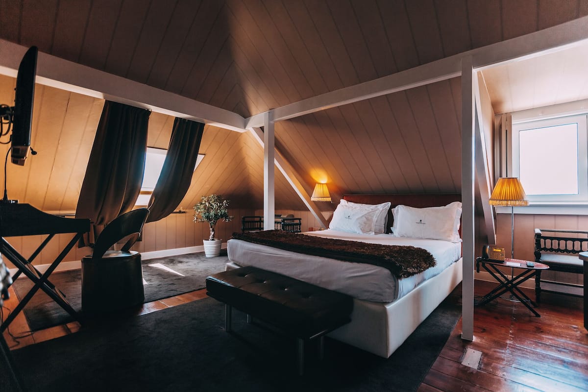 Une chambre à coucher avec un grand lit, un banc, une petite table et une lampe.