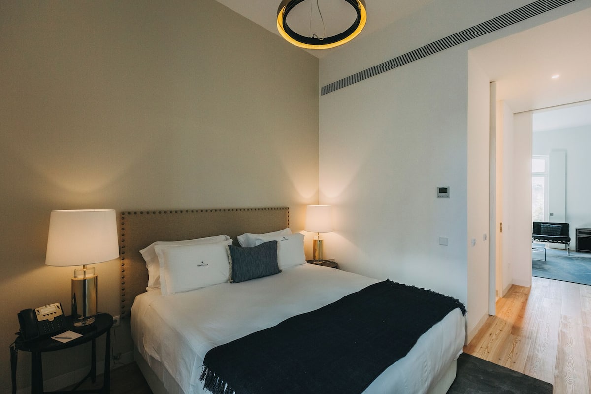 Une chambre d’hôtel comprenant un lit, deux tables de chevet avec des lampes, un téléphone et une porte donnant sur une autre pièce.