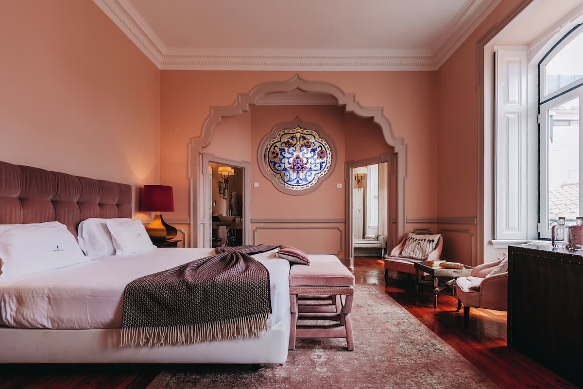 Une chambre à coucher avec un grand lit, une petite table, une chaise et une fenêtre décorative.