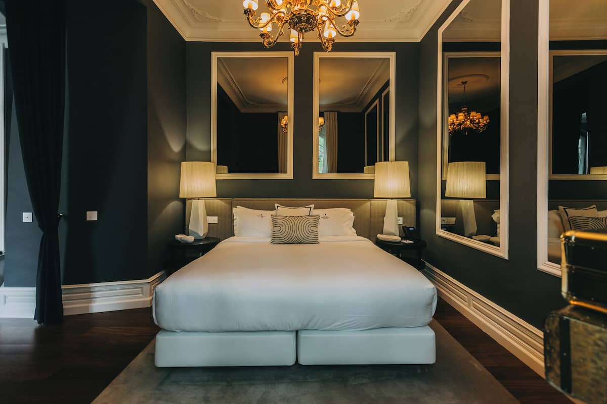 Un grand lit avec du linge de lit blanc, deux tables de chevet avec des lampes et un grand miroir au-dessus du lit.