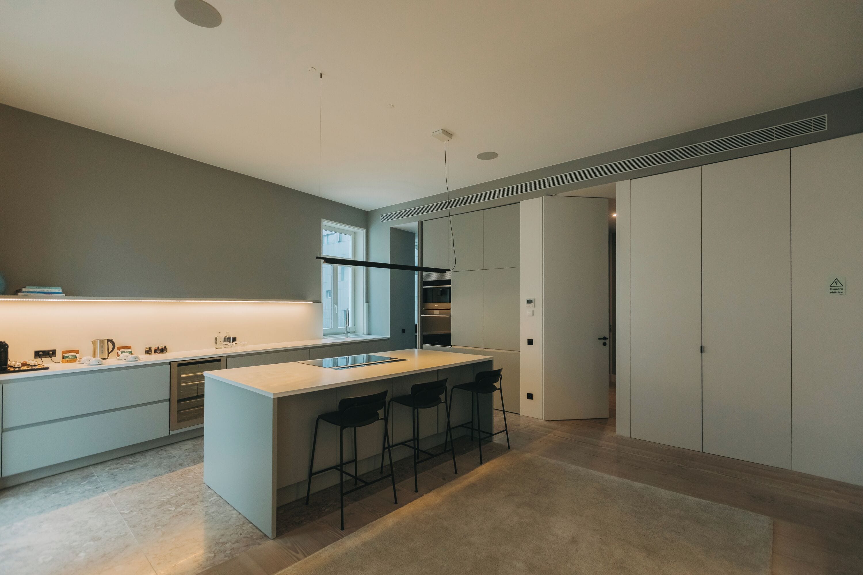 A modern kitchen with a central island, bar stools, and a large window.