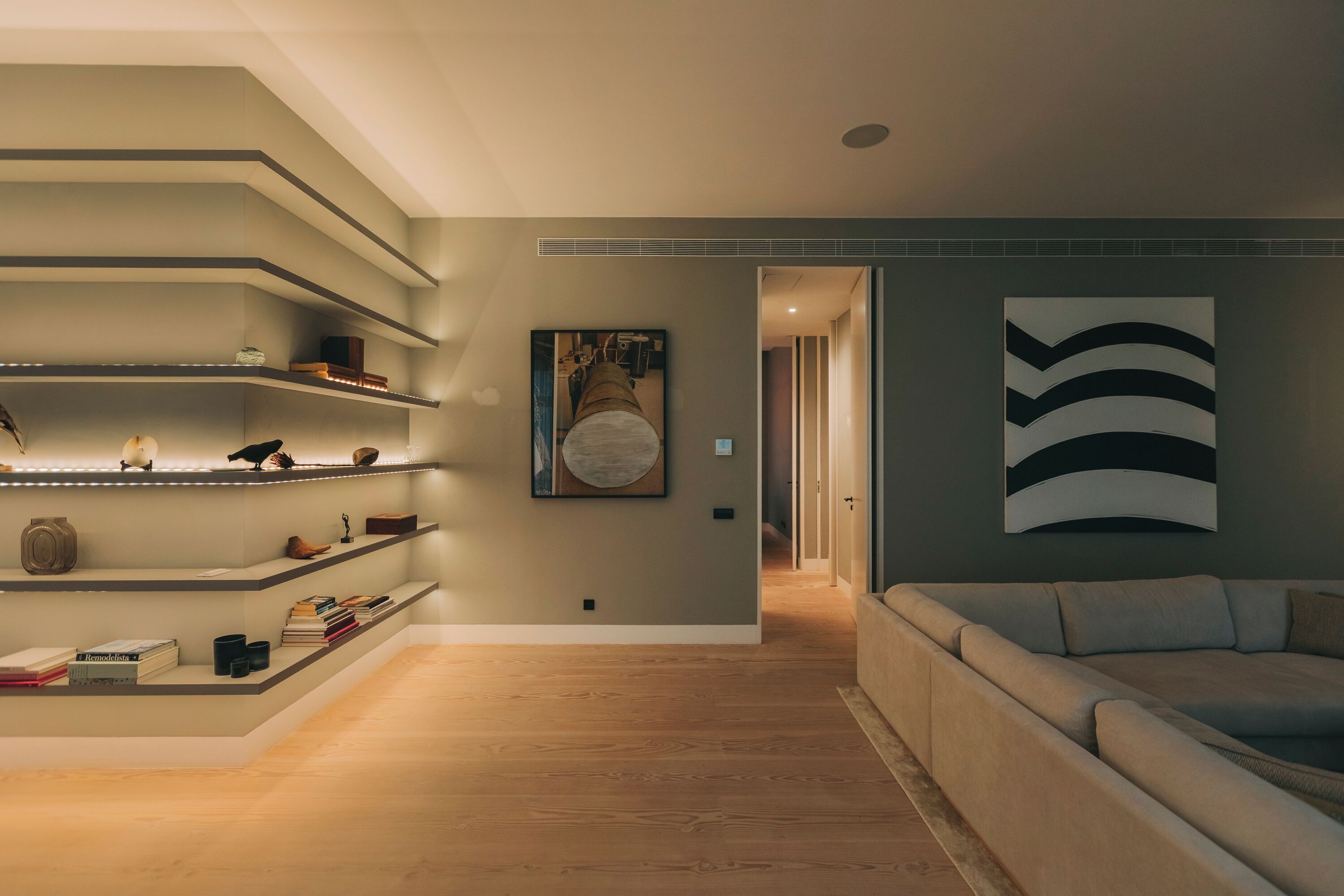 A modern living room with a sofa, wooden flooring, built-in shelves, and artwork on the walls.