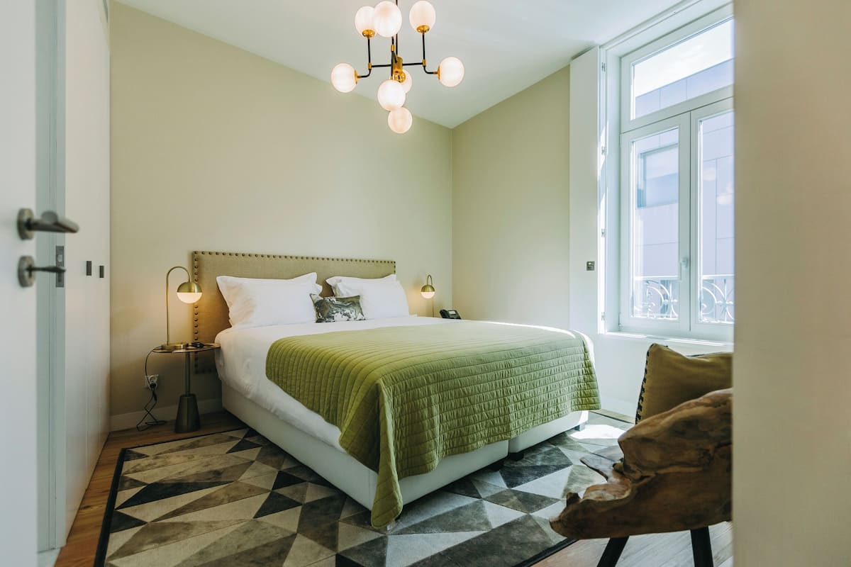 Une chambre à coucher avec un lit, un tapis à motifs géométriques, un lustre et une fenêtre donnant sur un beau paysage.