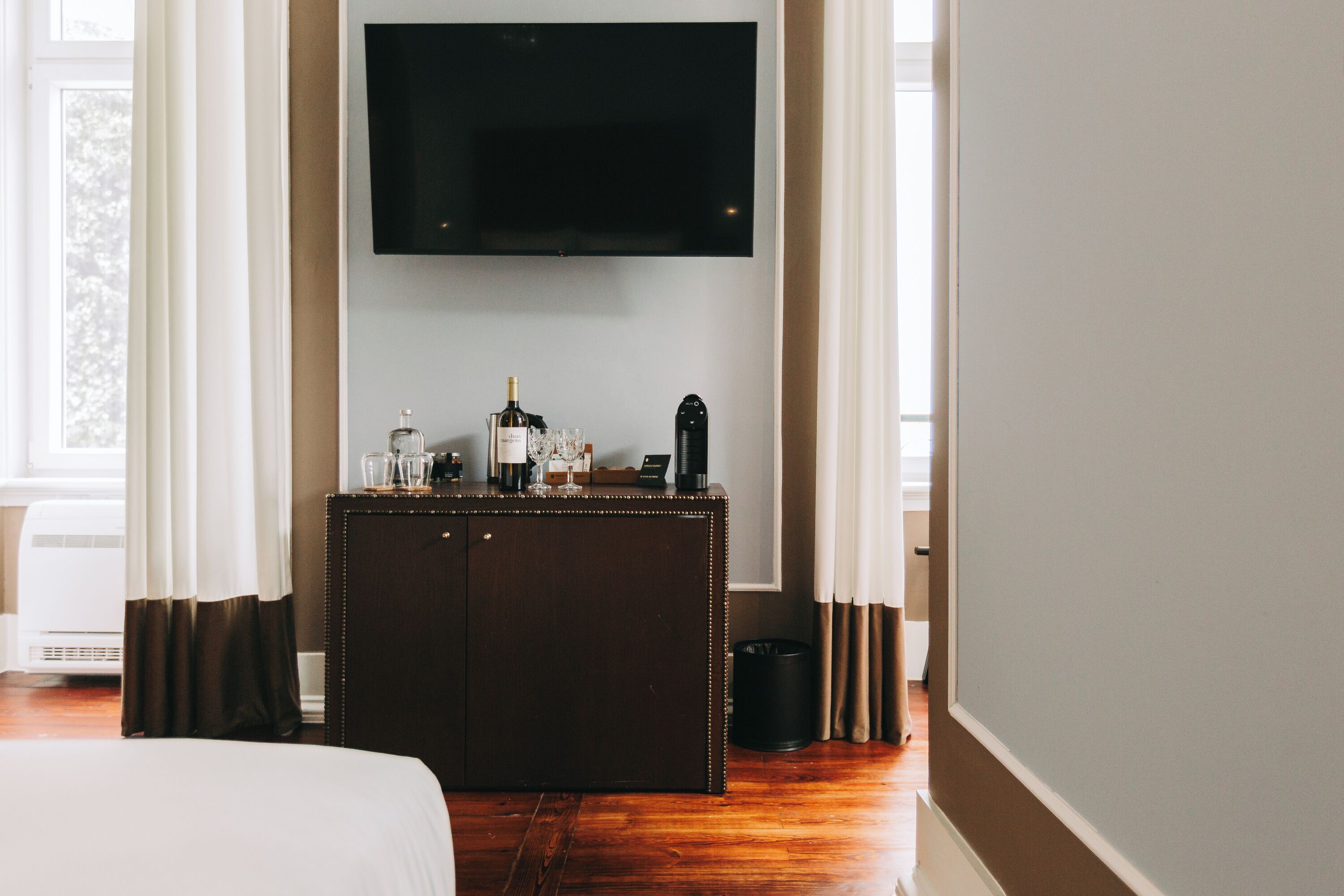 Une chambre d’hôtel avec une commode en bois, un téléviseur à écran plat fixé au mur et un lit recouvert d’une couette blanche.
