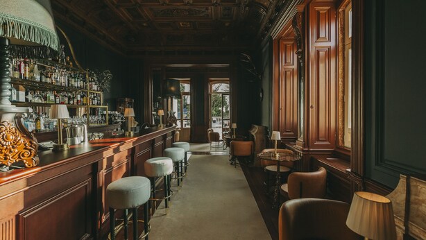 Zona de bar con mostrador de madera, taburetes y vistas a un espacio exterior a través de una puerta.