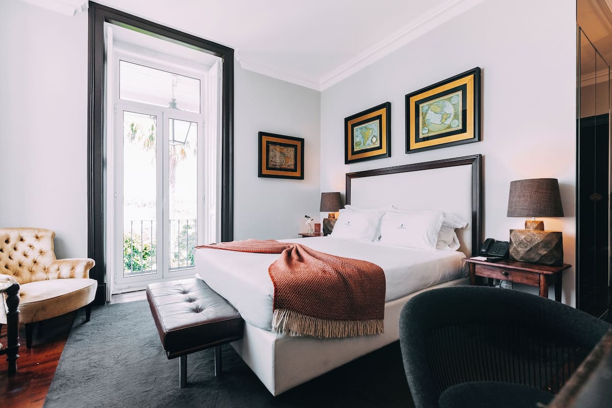 Une chambre d’hôtel avec un grand lit, une chaise, un banc, une table de chevet et une lampe.