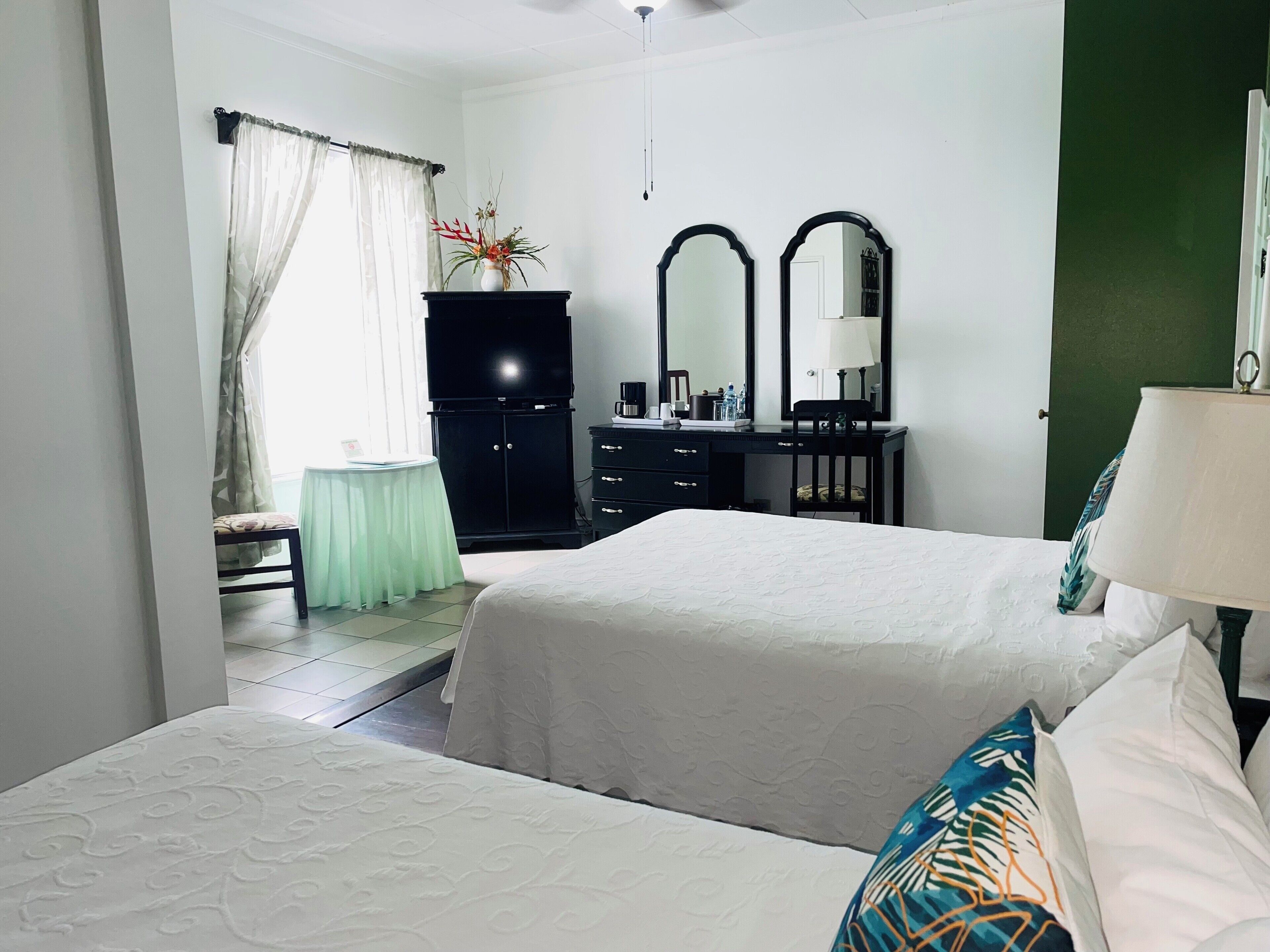 A hotel room with two beds, a desk with a lamp, a dresser, a TV, and a mirror.