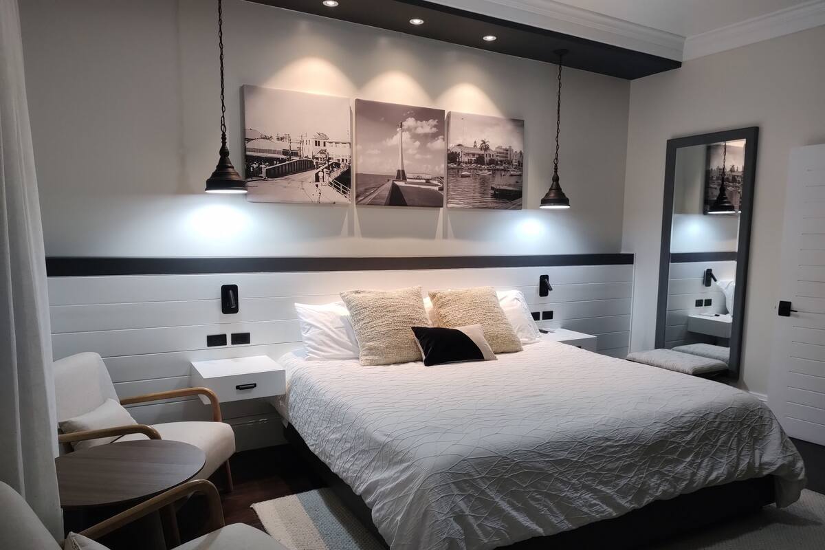 A modern bedroom with a large bed, bedside tables, a chair, and a mirror.
