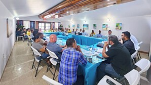 Un salón de conferencias con una larga mesa, sillas blancas y un mantel azul.
