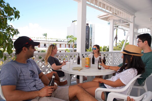 A group of people sitting at a round table with drinks and a bottle of Zone beer, under a white pergola with a view of buildings and palm trees. - The Great House (Belize City)