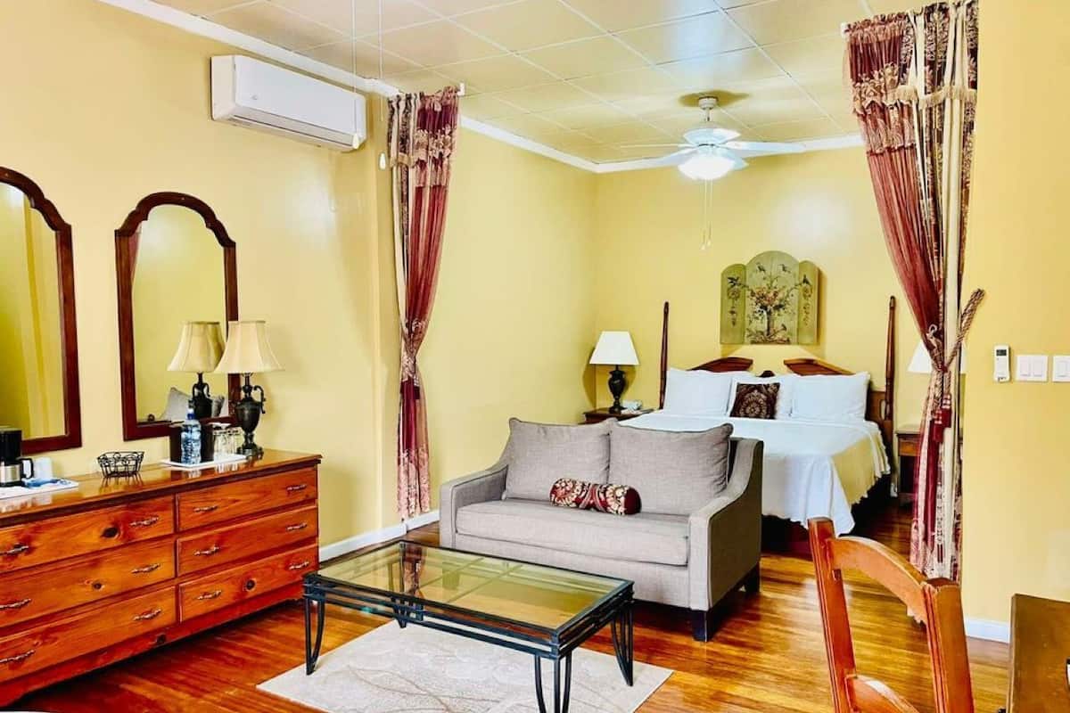 A living room with a sofa, a glass coffee table, a wooden dresser, and a bed with a canopy.
