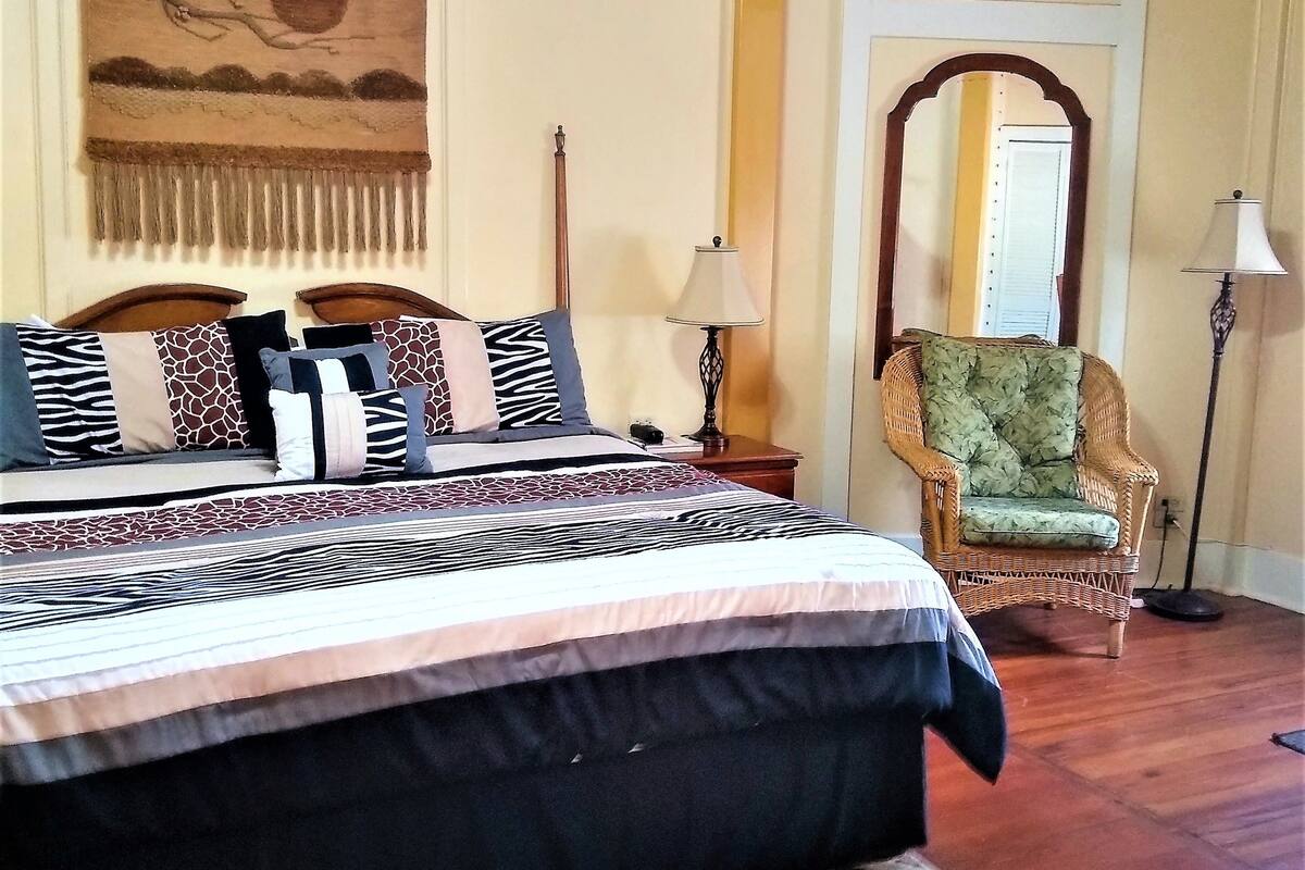 A bedroom with a large bed, a chair, a lamp, and a mirror.