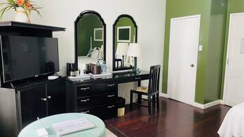 A hotel room with a TV, a desk with a mirror, a chair, a small table with a menu, and a vase with flowers.