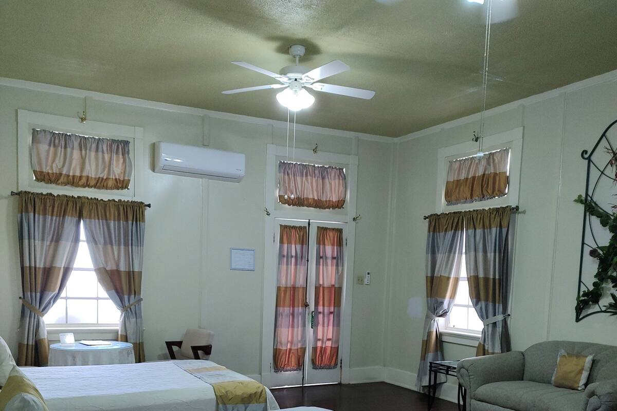 A hotel room with two beds, a ceiling fan, a sofa, and a small table.
