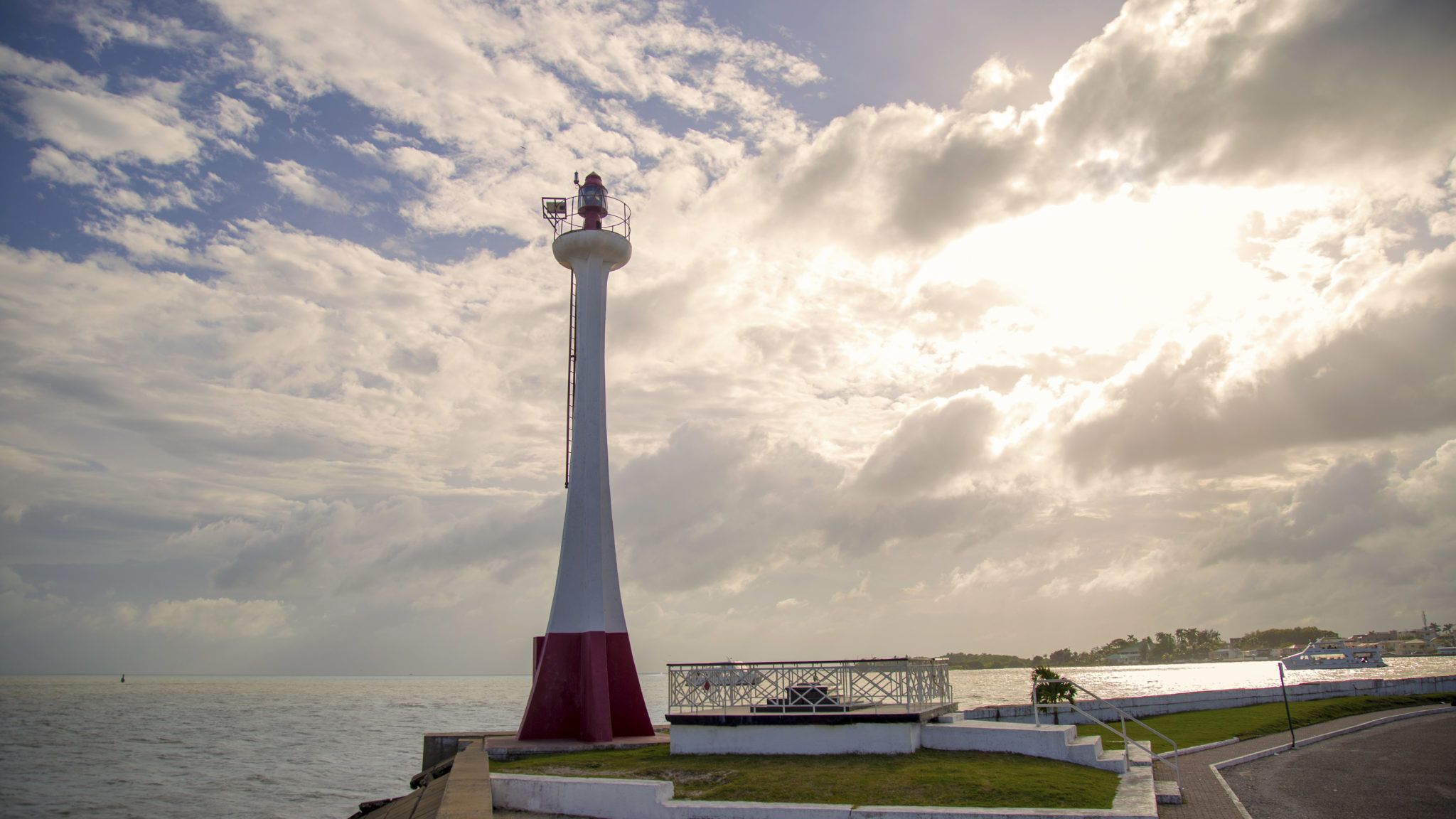 A lighthouse with a white and red base, situated by the water with a cloudy sky in the background.