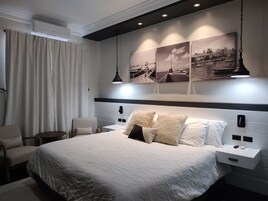 Una habitación de hotel moderna con una cama grande, una silla, una mesita de noche y una lámpara fijada a la pared.