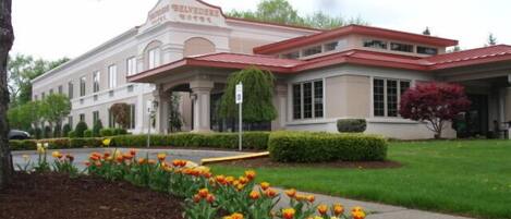 A hotel with a classic architectural style, featuring a central entrance with columns, a red roof, and a well-maintained garden with tulips.