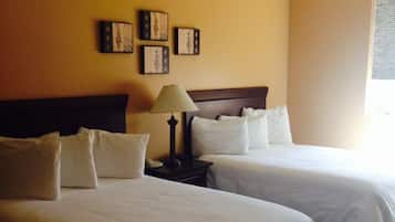 Habitación de hotel con dos camas, una mesita de noche con lámpara y cuadros en la pared.